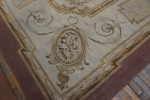 Ornate low-pile rug in cream and brown tones featuring a floral medallion detail on distressed wood planks.