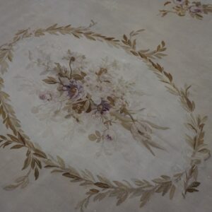 Pale rug detail showing a central floral bouquet encircled by brown and tan leafy vines.