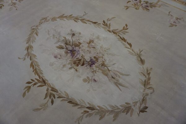 Pale rug detail showing a central floral bouquet encircled by brown and tan leafy vines.