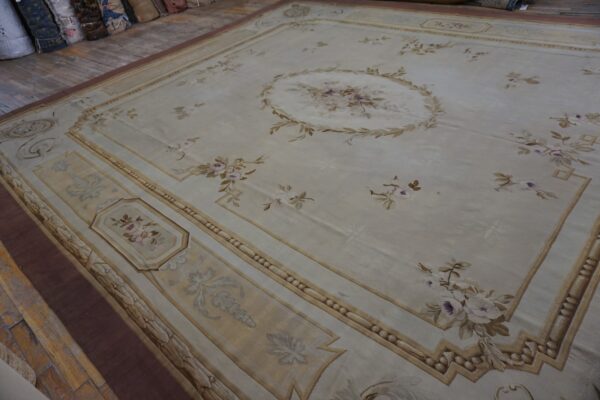 Large pale cream rug with a central floral medallion and ornate architectural borders, displayed on distressed wood flooring.