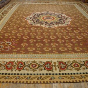 Large sienna-toned rug featuring a star medallion and intricate borders in red, cream, gold, and teal on wood flooring.