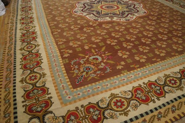 Intricate traditional rug with a brown field, center medallion, and wide borders displayed on wood floor.