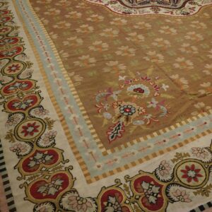 Detailed view of a low-pile rug with a brown field, small florals, and wide multi-banded red and cream borders.
