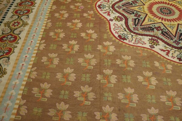 Detailed low-pile rug with a brown background, bright floral motifs, and elaborate borders in red, teal, and cream.
