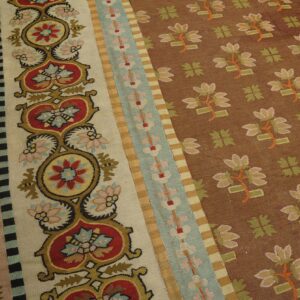 Close-up of a flatweave rug with a brown floral field and intricate striped borders in cream, red, blue, and yellow.