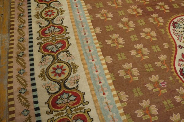 Close-up of a flatweave rug with a brown floral field and intricate striped borders in cream, red, blue, and yellow.