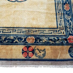 Close-up of a cream and gold high-pile rug featuring blue Greek key borders and floral medallions.