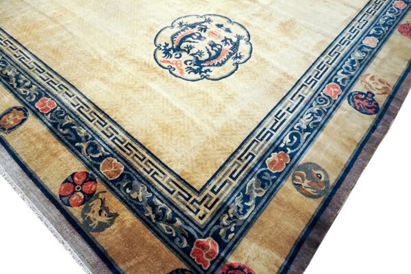 The corner of a pale gold rug showing blue borders, red flowers, and a central blue dragon motif.