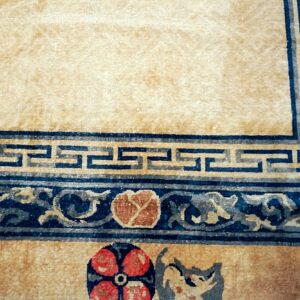 Tan rug with dark blue borders; patterns include Greek key, scrolling vines, and red floral motifs.