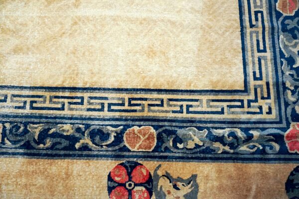 Tan rug with dark blue borders; patterns include greek key, scrolling vines, and red floral motifs.