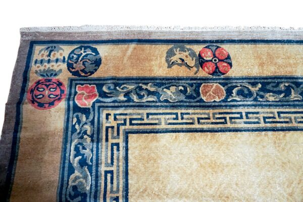 Tan and dark blue rug corner showing a geometric key border, scrolling vines, and round red floral motifs.