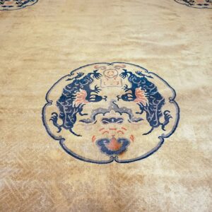 Low-pile beige rug featuring a circular dark blue, orange, and gray stylized creature motif.