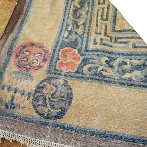 Tan rug with dark blue geometric borders, stylized circular designs, and short visible fringe.