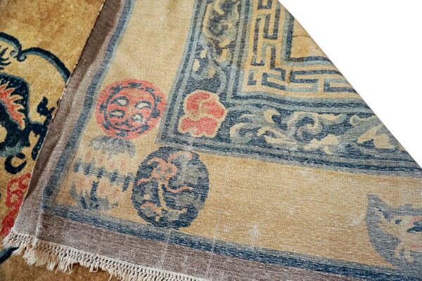 Tan rug with dark blue geometric borders, stylized circular designs, and short visible fringe.