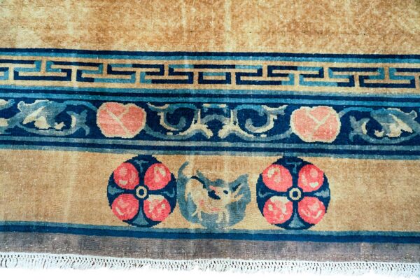 Tan rug detail with borders featuring navy and light blue greek key, coral florals, and a central animal motif.