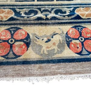 Close-up of a low-pile tan, blue, and coral rug featuring floral medallions and an animal design near the fringe.