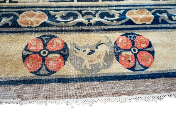 Close-up of a low-pile tan, blue, and coral rug featuring floral medallions and an animal design near the fringe.
