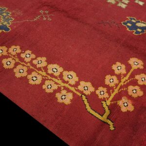 Close-up of a deep red rug featuring stylized floral motifs in yellow, pink, and dark blue.
