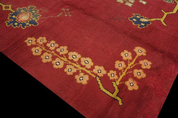 Close-up of a deep red rug featuring stylized floral motifs in yellow, pink, and dark blue.