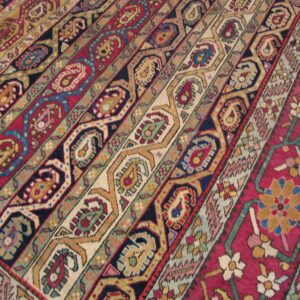 Colorful low-pile rug detail featuring diagonal stripes of geometric and stylized paisley motifs in red, blue, and gold.