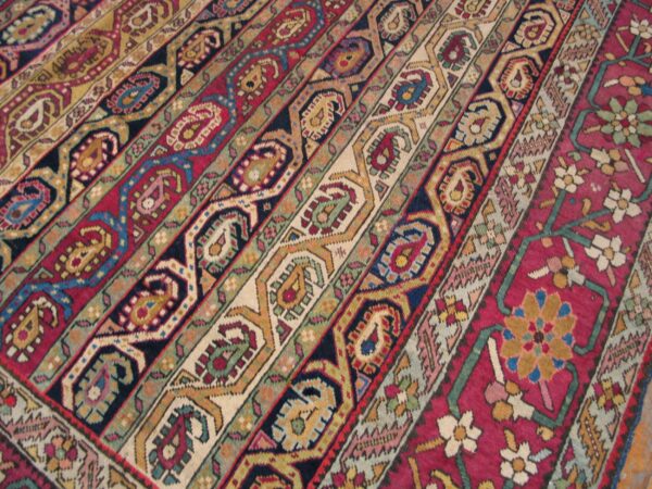 Colorful low-pile rug detail featuring diagonal stripes of geometric and stylized paisley motifs in red, blue, and gold.