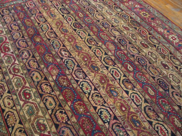 Rug with colorful red, gold, and navy vertical stripes of intricate paisley and geometric designs on a wood floor.