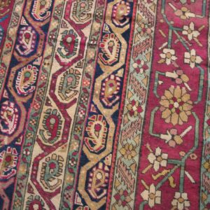 Rug detail showing vertical bands of red, blue, and tan geometric patterns next to a magenta floral section.