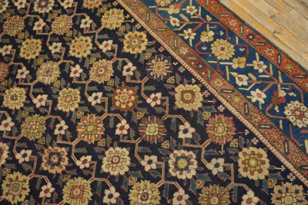 Navy rug with a dense gold and red floral pattern and multi-banded border rests on wood planks.