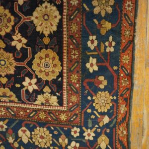 A close-up of a blue, gold, and red floral patterned rug resting on distressed yellow wood planks.