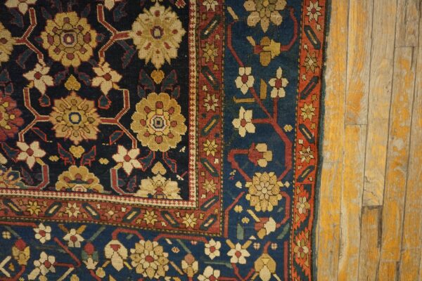A close-up of a blue, gold, and red floral patterned rug resting on distressed yellow wood planks.