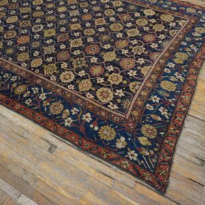Dark blue rug with red and gold stylized flowers and borders covers worn wooden plank flooring.