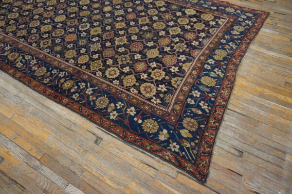 Dark blue rug with red and gold stylized flowers and borders covers worn wooden plank flooring.