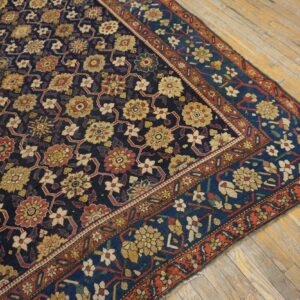 Low-pile rug with navy, gold, and red floral lattice pattern on worn natural wood floorboards.