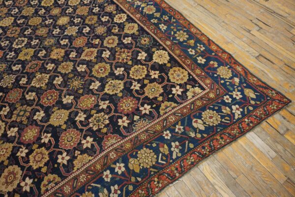 Low-pile rug with navy, gold, and red floral lattice pattern on worn natural wood floorboards.