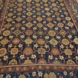 Dark blue rug featuring a repeating pattern of gold, red, and cream florals on light wood floors.