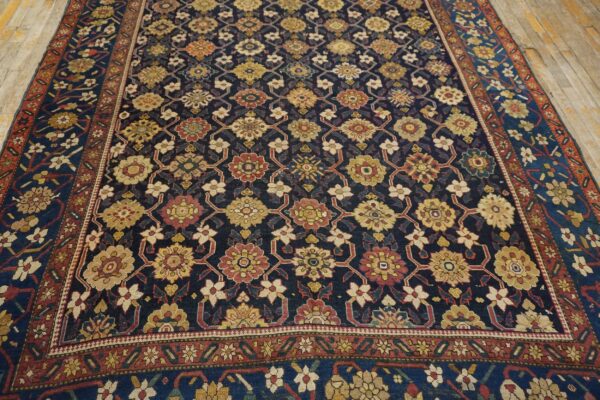 Dark blue rug featuring a repeating pattern of gold, red, and cream florals on light wood floors.