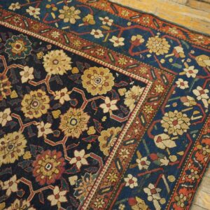 Ornate dark blue rug with red and gold floral lattice patterns shown on light distressed hardwood floors.