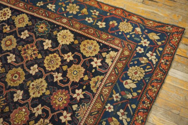 Ornate dark blue rug with red and gold floral lattice patterns shown on light distressed hardwood floors.