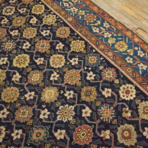 Navy blue rug featuring intricate yellow, red, and beige floral patterns, bordered by bright blue and rust, on wood flooring.