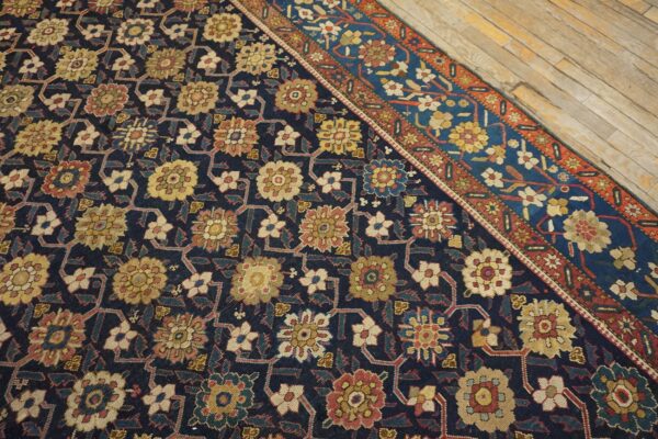 Navy blue rug featuring intricate yellow, red, and beige floral patterns, bordered by bright blue and rust, on wood flooring.