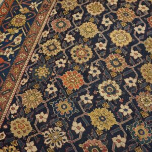 Dark navy rug featuring a repeating lattice of stylized yellow, red, and cream flowers on distressed wood flooring.