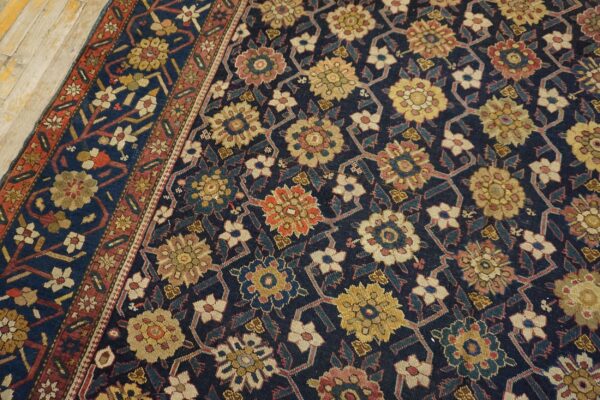 Dark navy rug featuring a repeating lattice of stylized yellow, red, and cream flowers on distressed wood flooring.