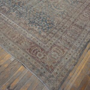 Distressed traditional rug featuring faded blue and beige floral patterns sits on patchy wood flooring.