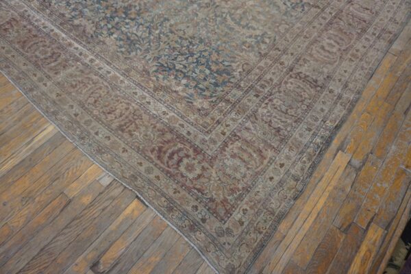 Distressed traditional rug featuring faded blue and beige floral patterns sits on patchy wood flooring.