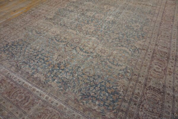 Muted traditional rug displaying dense floral patterns in dusty teal, beige, and rust on wood floors.