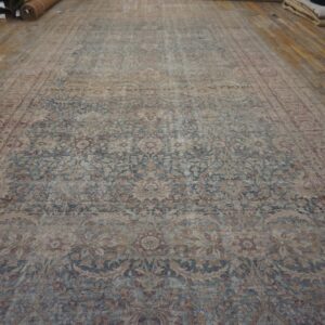 Distressed rug with intricate blue and beige botanical designs displayed on wide wood plank flooring.