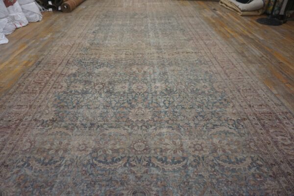 Distressed rug with intricate blue and beige botanical designs displayed on wide wood plank flooring.