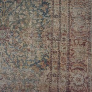 Distressed traditional rug with low pile, showing faded blue, red, and tan floral designs on wood flooring.