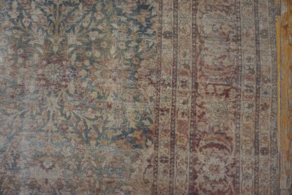 Distressed traditional rug with low pile, showing faded blue, red, and tan floral designs on wood flooring.