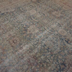 Faded traditional rug in beige, blue, and maroon laying on a light wooden floor.
